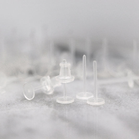 A set of clear plastic earring posts with rubber earring backs placed on a surface.