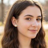 Close-up of an ear wearing two earrings: a small stud and a larger, colorful round mermaid scale earring.