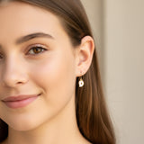Close-up of an ear wearing a gold 'D' earring with a clear gemstone.