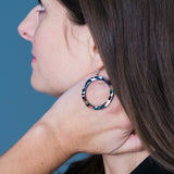 Close-up of a woman wearing colorful hoop earrings against a blue background
