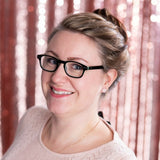 Woman wearing glasses and a light sweater with a pink curtain background and 10mm round rose quartz earrings