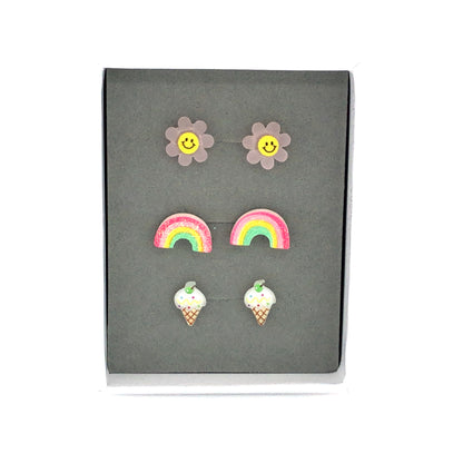 Three pairs of earrings displayed in a box, featuring a pink smiley face, a multicolored rainbow, and a vanilla ice cream cone design.