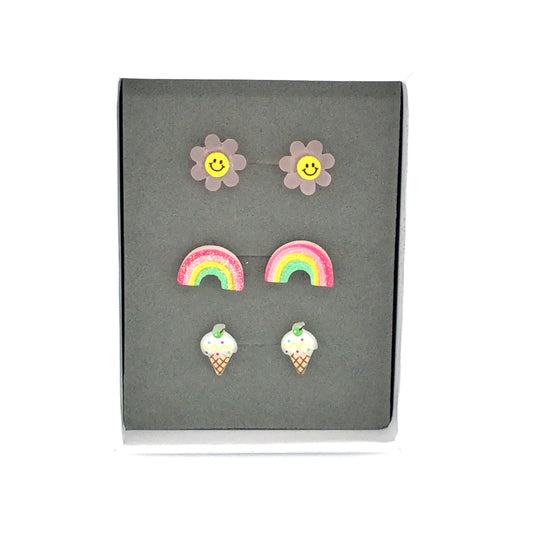 Three pairs of earrings displayed in a box, featuring a pink smiley face, a multicolored rainbow, and a vanilla ice cream cone design.