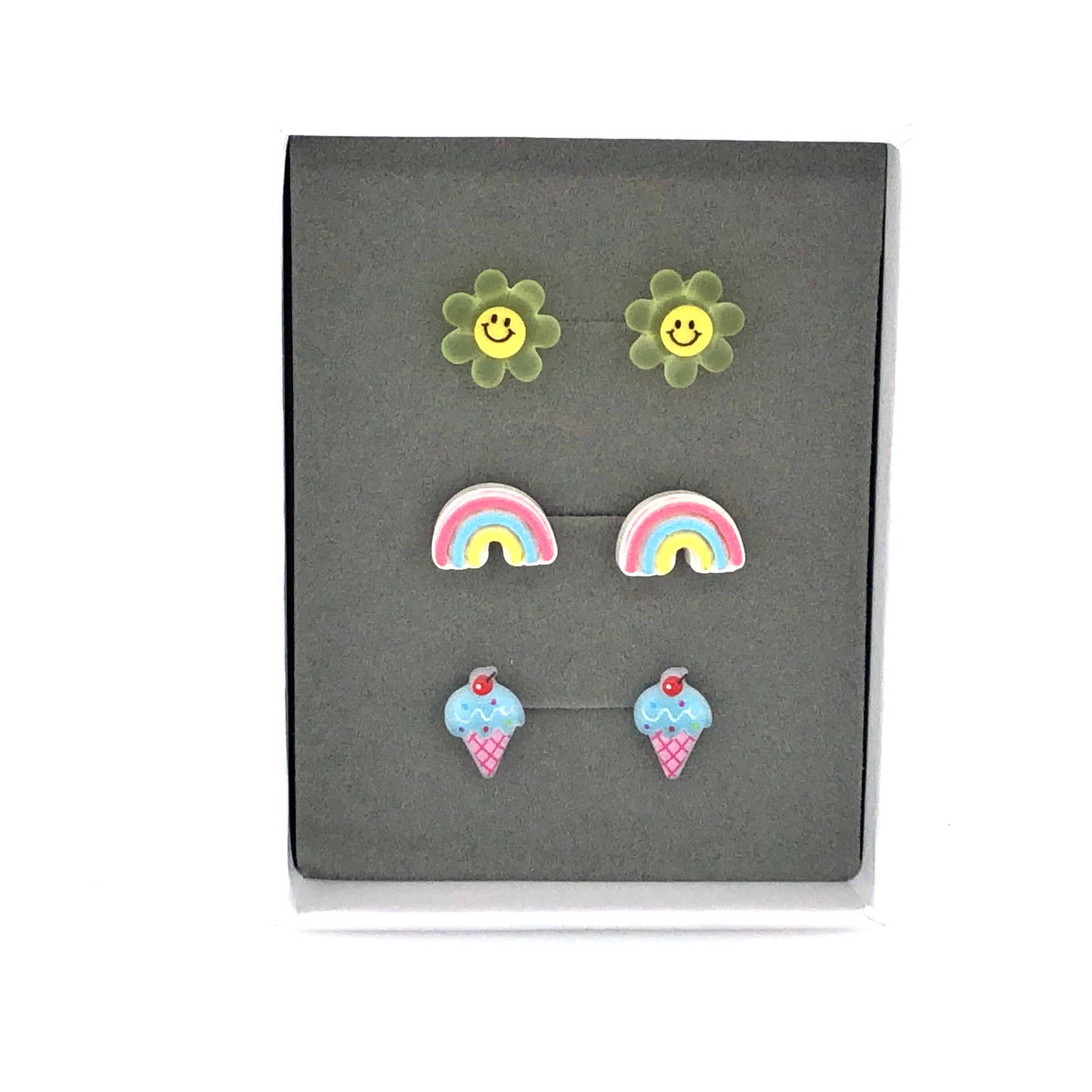 Three pairs of earrings displayed in a box, featuring a yellow smiley face, a pastel rainbow, and a blue ice cream cone design.