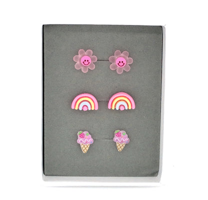 Three pairs of earrings featuring a dark pink smiley face daisy, a pink rainbow, and a purple ice cream cone design, presented in a box 