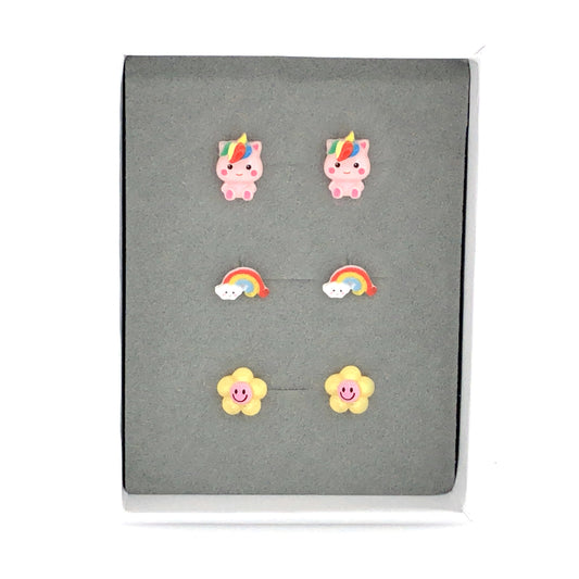 A set of three pairs of stud earrings featuring a pink rainbow unicorn, a dainty rainbow with cloud, and a yellow and pink smiley face flower, presented in a grey box.