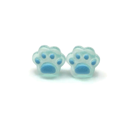 A pair of dainty paw print-shaped stud earrings in a beige color with brown details on a white background.
