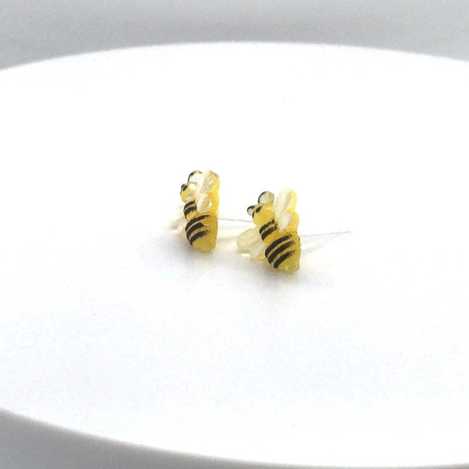 A pair of bee-shaped stud earrings made of resin, with yellow and black color scheme, displayed against a white background.