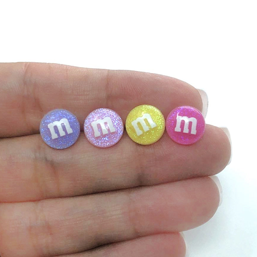purple, light pink, yellow and dark pink M&M candy earrings in a hand