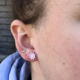 Close-up of an ear with a flower-shaped earring and a small stud earring.
