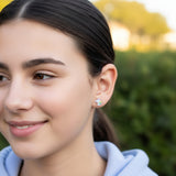 Close-up of an ear with two earrings: a unicorn-shaped earring and a small round crystal earring.