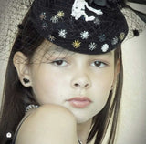 Young girl wearing a decorative black hat with embellishments and black bat earrings