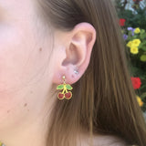 Close-up of an ear wearing a cherry-themed earring with a blurred background