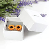 Sunflower-shaped earrings in a white box with branding, surrounded by lavender flowers.