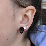 Close-up of an ear with black skull earring and clear gemstone earring.