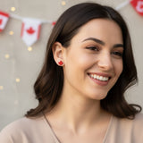 Close-up of an ear with a red maple leaf earring and a clear gemstone earring.