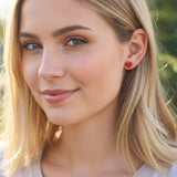 Close-up of a person wearing a red heart-shaped earring with a blurred background