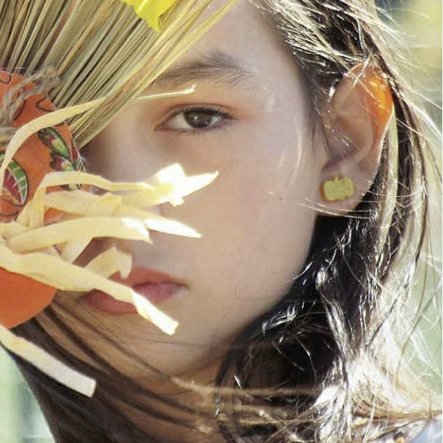 Close-up of a person wearing glitter pumpkin earrings with a blurred background
