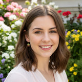 Close-up of a person wearing a cherry-shaped earring with a blurred floral background