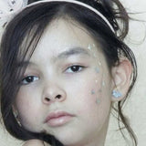 Young girl with glitter on her face and silver glitter bunny earrings against a neutral background
