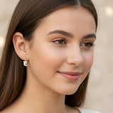 Close-up of an ear wearing a gold letter 'E' earring with a blurred background