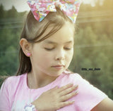 Young girl with a colorful bow in her hair, wearing a pink shirt, outdoors with pink cat earrings