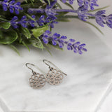 Silver floral earrings on a white surface with lavender flowers in the background