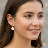 Close-up of an ear wearing a gold flower-shaped earring with a blurred background