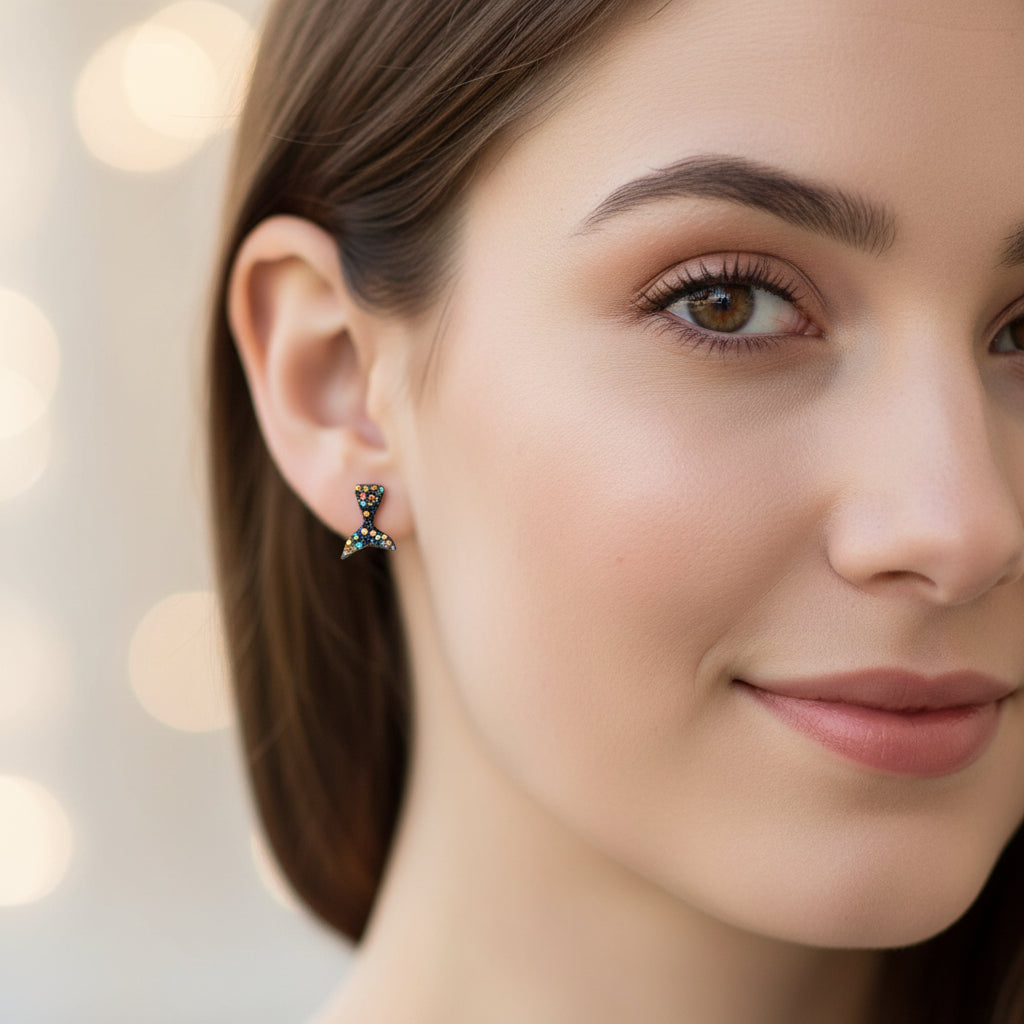 Close-up of an ear wearing a colorful black glitter mermaid tail earring with a blurred background