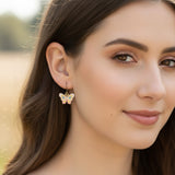 Butterfly earrings worn by a person with a blurred outdoor background