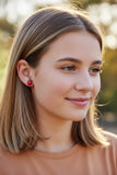 Close-up of a person wearing a red ladybug earring with a black dot.