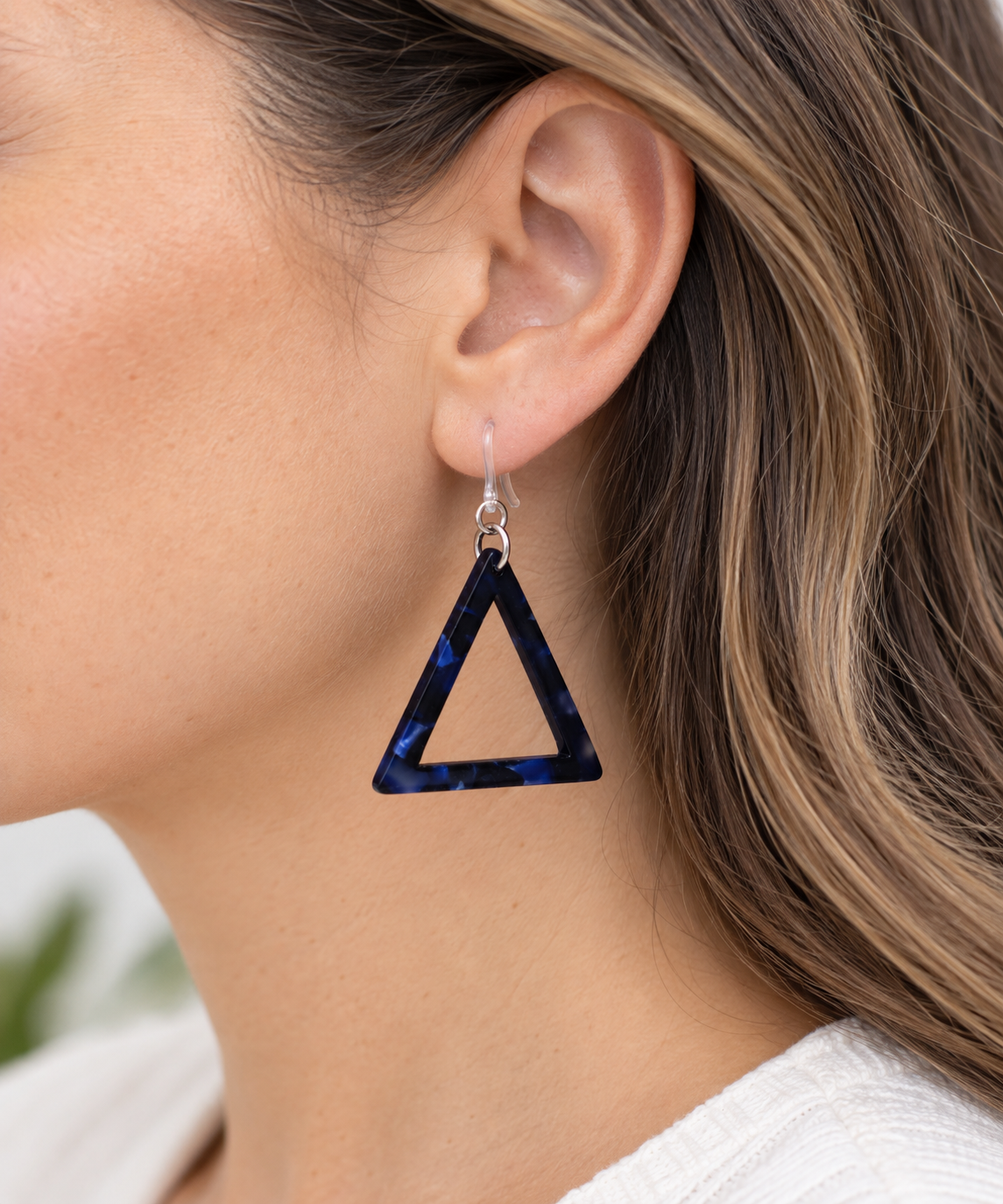 A close-up of a woman's ear wearing a triangular drop earring made of dark blue marbled resin with silver hooks.