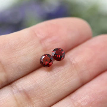 A pair of red cubic zirconia stud earrings mounted on a gold-colored post, part of the Birthstone Collection for April.