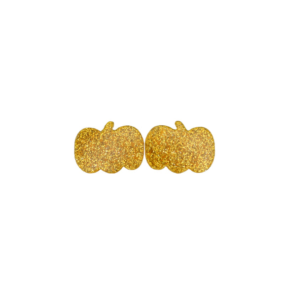Gold glittery pumpkin-shaped earrings on a white surface with green leaves in the background