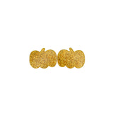 Gold glittery pumpkin-shaped earrings on a white surface with green leaves in the background