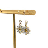 A pair of dangle earrings featuring a white and yellow daisy design on a silver hook.