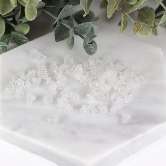 A collection of clear rubber ear nut backs for earrings displayed on a white surface, with green leaves in the background.