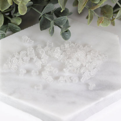 Clear soft rubber earring backs arranged on a white surface, intended for use with plastic posts.