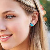 Close-up of a person wearing turquoise heart-shaped earrings with blurred background