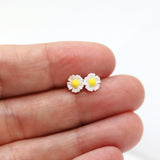 White daisy flower earrings held between fingers on a white background