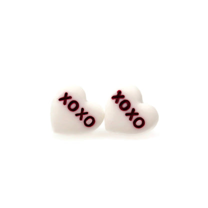 A pair of pink conversation heart stud earrings with the phrase 'BE MINE' printed on them.