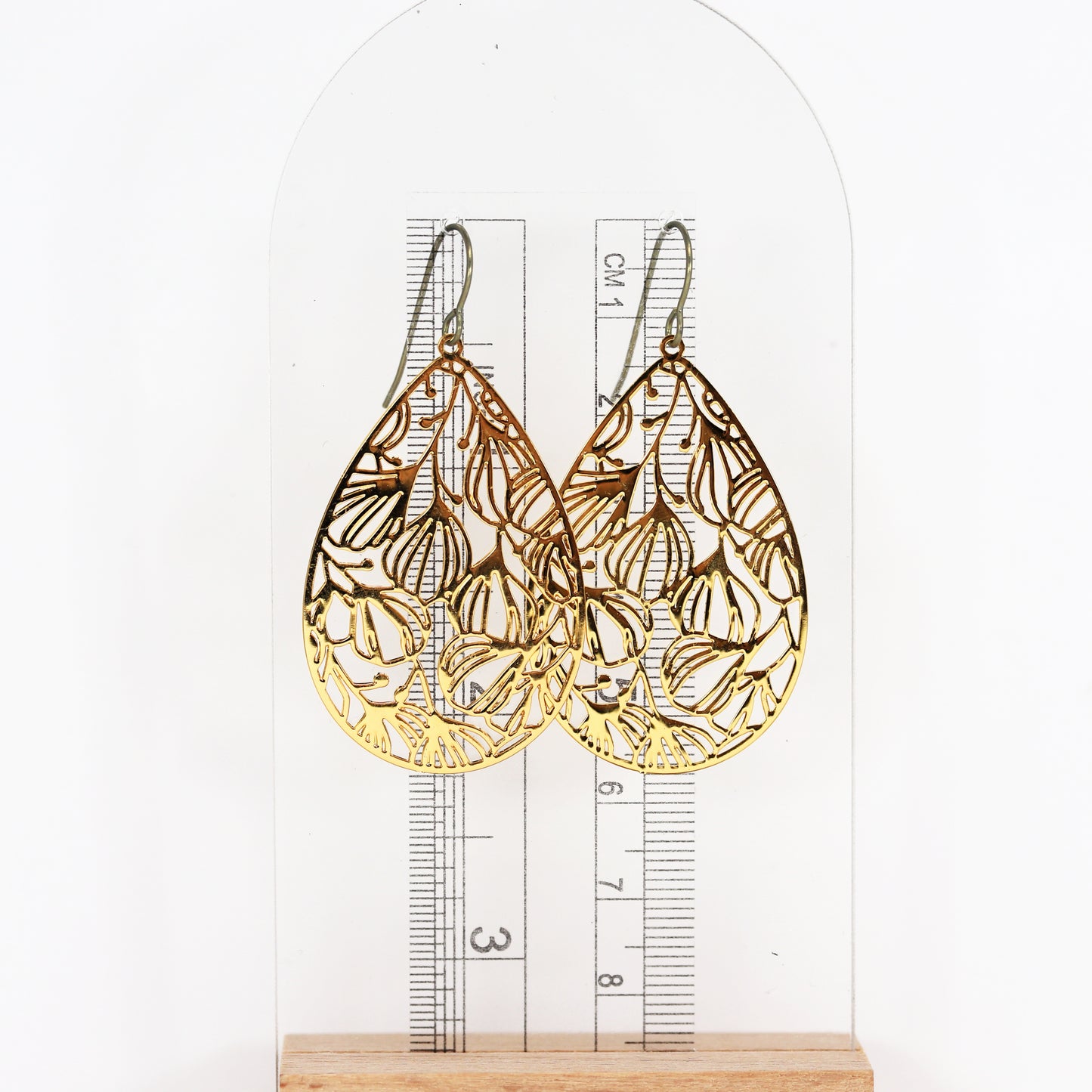 A pair of gold floral filigree teardrop dangle earrings with a polished stainless steel finish, designed for invisible clip-on wear.
