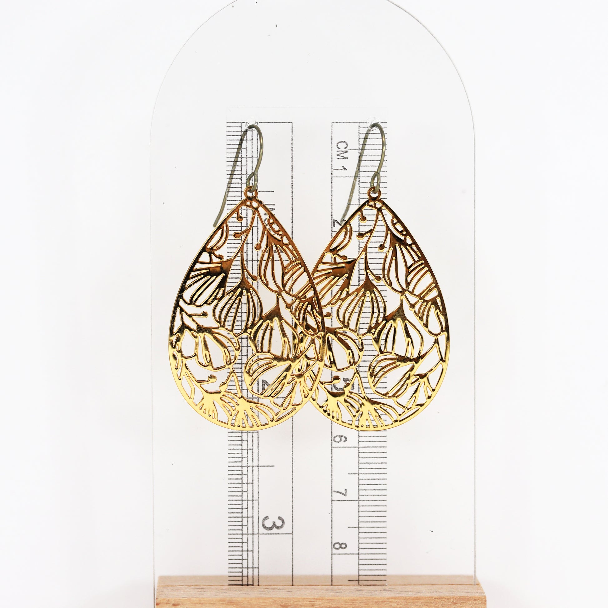 A pair of gold floral filigree teardrop dangle earrings with a polished stainless steel finish, designed for invisible clip-on wear.