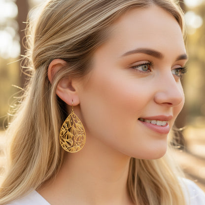 A pair of gold floral filigree teardrop dangle earrings with a polished stainless steel finish, designed for invisible clip-on wear.