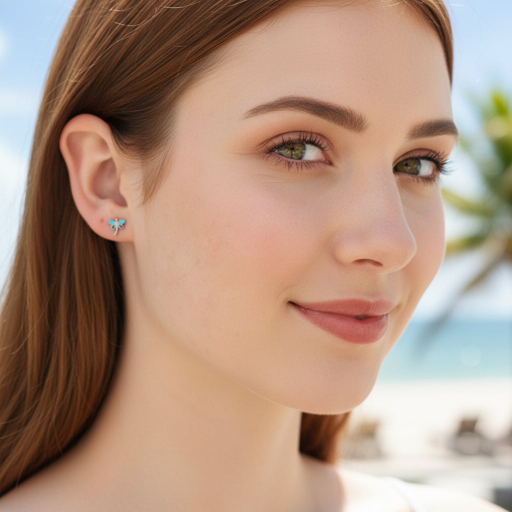 A pair of stainless steel dainty dragonfly stud earrings with a blue and gold PVD coating, featuring flat screw-on backs.