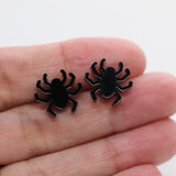 Black spider earrings held in a hand on a white background