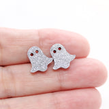 Silver ghost-shaped earrings held between fingers on a white background
