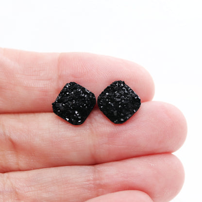 A pair of black square druzy stud earrings with rounded corners on a white background