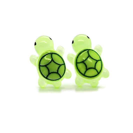 A pair of green turtle stud earrings made of resin, designed with black patterns on the turtle shells.