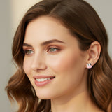 Two small cow-shaped earrings held between fingers on a white background
